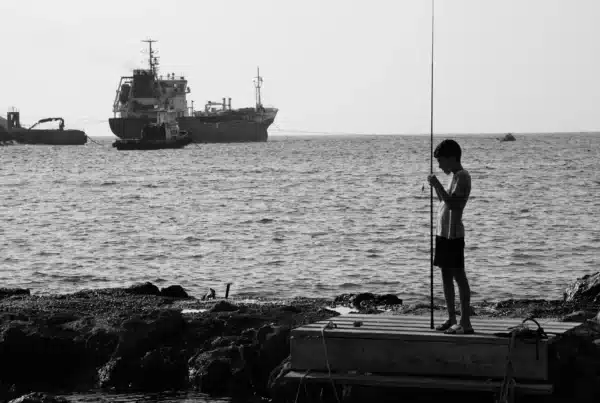 vedant system fotografia czarno - biała, chłopak łowi ryby w morzu, tankowiec