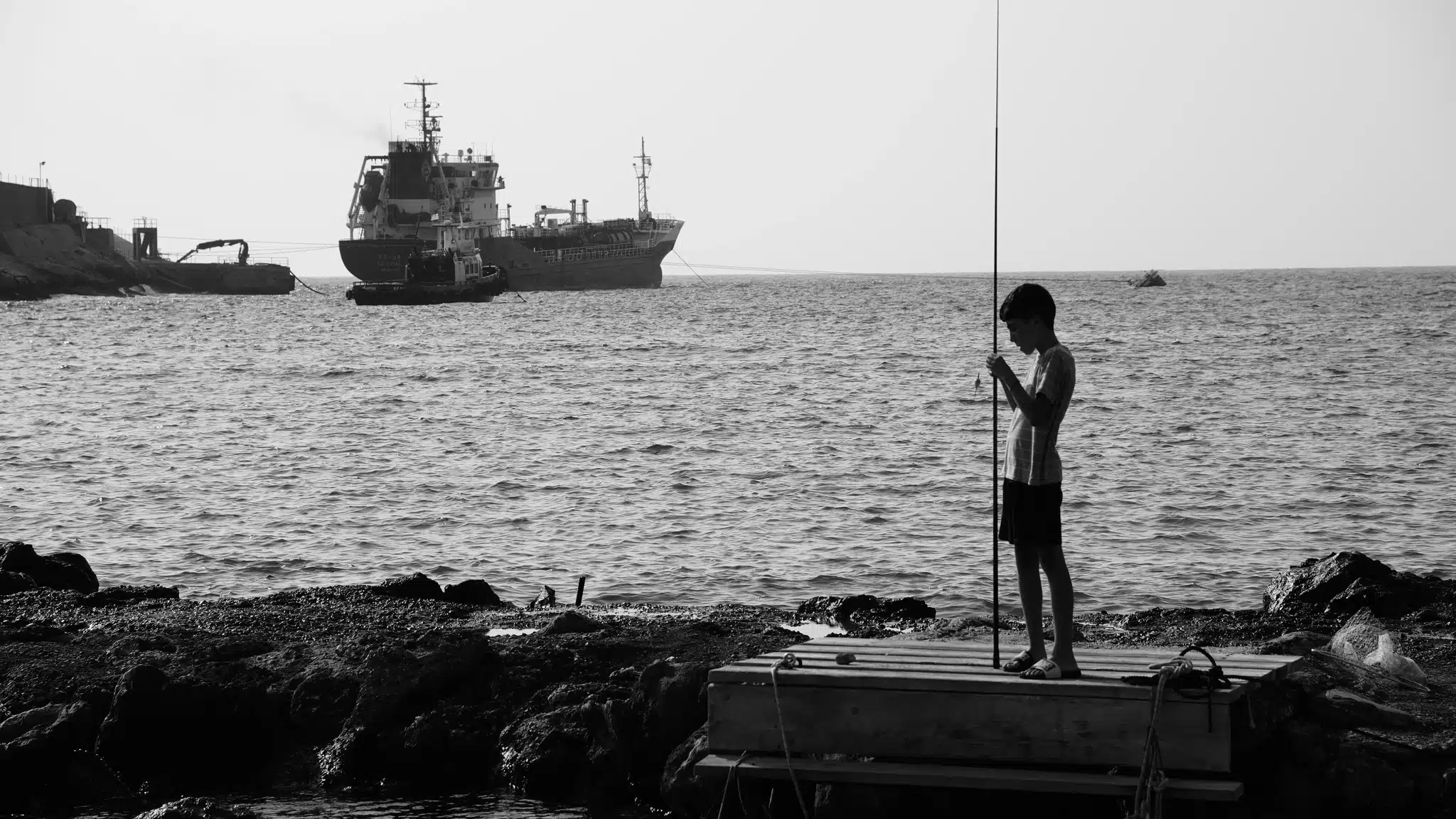 vedant system fotografia czarno - biała, chłopak łowi ryby w morzu, tankowiec